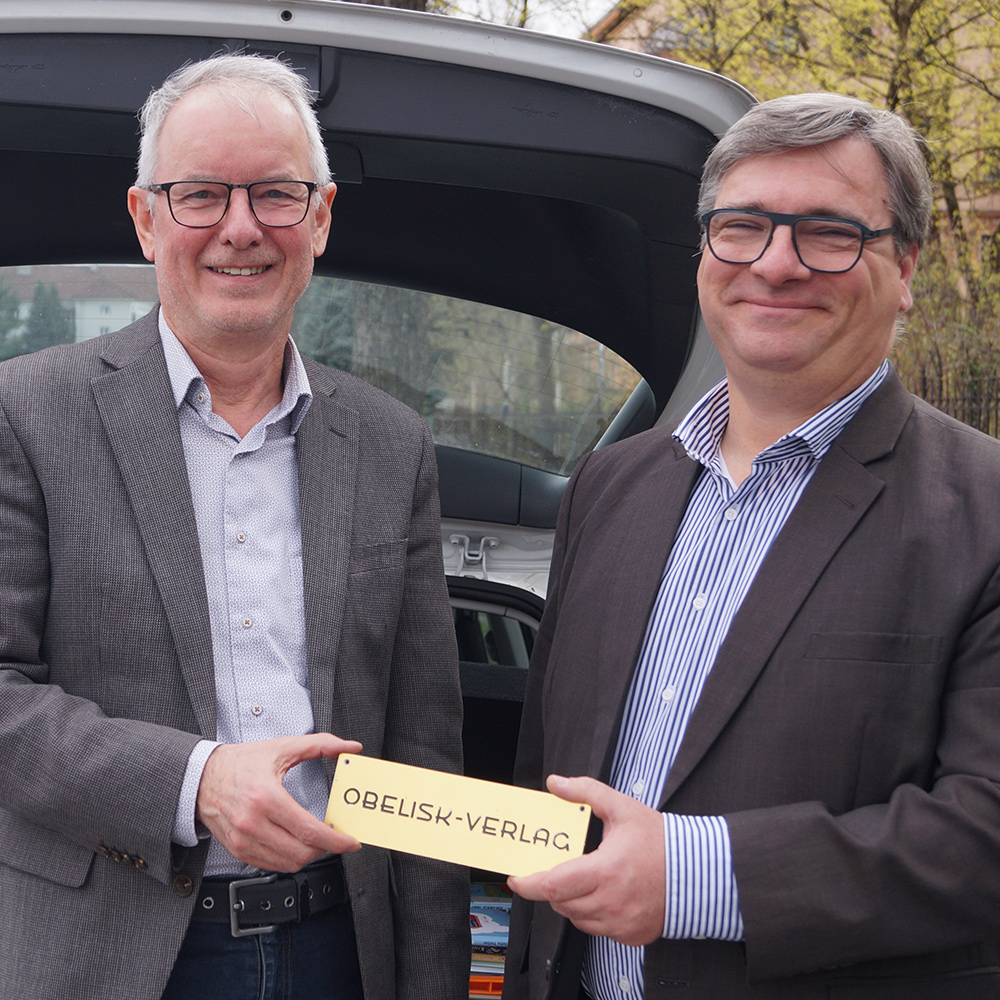 Mag. Gottfried Kompatscher und Ing. Markus Buchroithner mit dem Obelisk-Firmenschild | © Tyrolia Verlag
